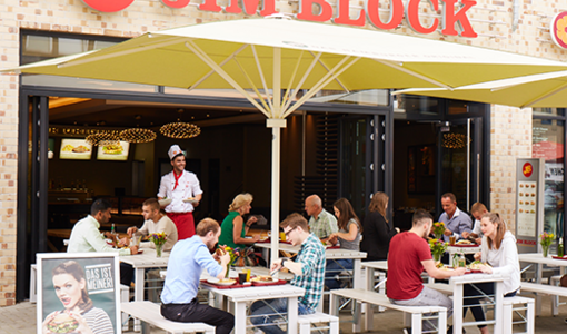 Jim Block Restaurant mit einer Terrasse wo Gäste unter Sonnenschirmen sitzen und Essen
