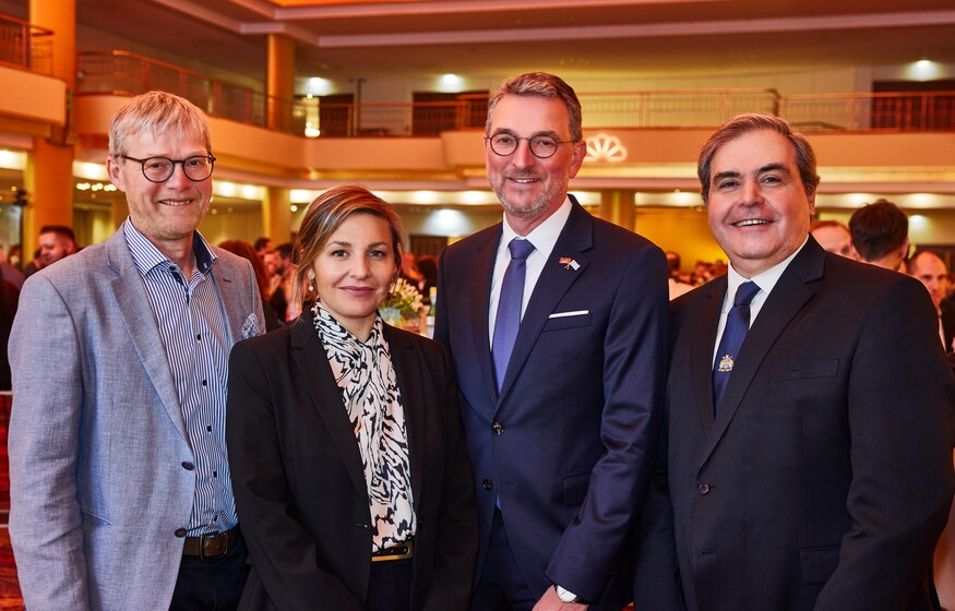 Eine Gruppe von vier Menschen steht im Festsaal des Grand Elysée Hamburg. Es gibt eine Frau und drei Männer, alle sind in eleganter Abendkleidung gekleidet.