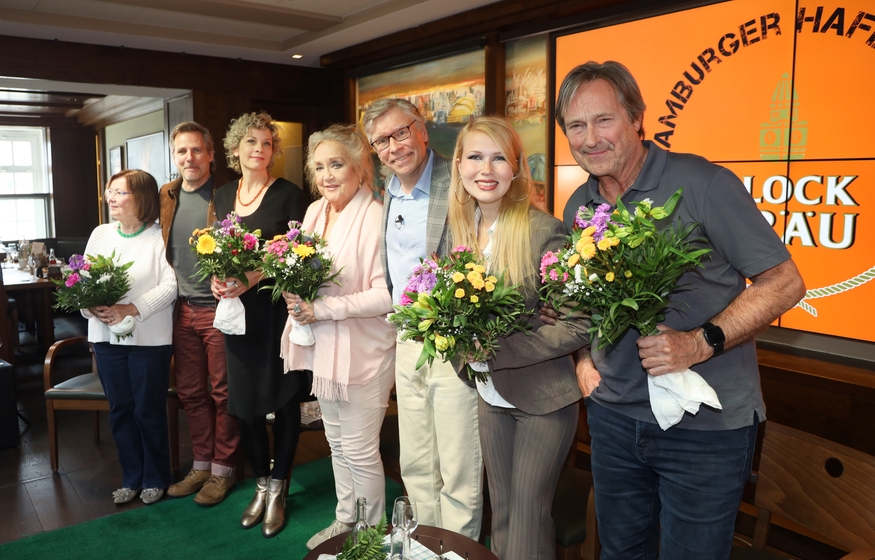 Alle 7 Teilnehmer des 14. Hamburger Hafen Talks (v.l. Herma Koehn, René Steinke, Anna Schäfer, Doris Kunstmann, Thorsten Laussch, Alexandra Rotmann und Helmut Zierl) auf der Bühne des BLOCKBRÄU, lächelnd und mit Blumensträußen in der Hand haltend.