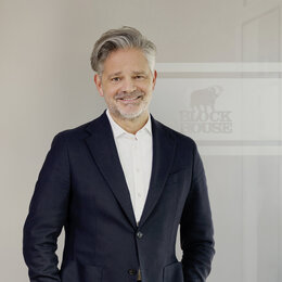 Carsten Horn im dunklen Anzug und weißem Hemd. Er hat graue Haare und einen Bart