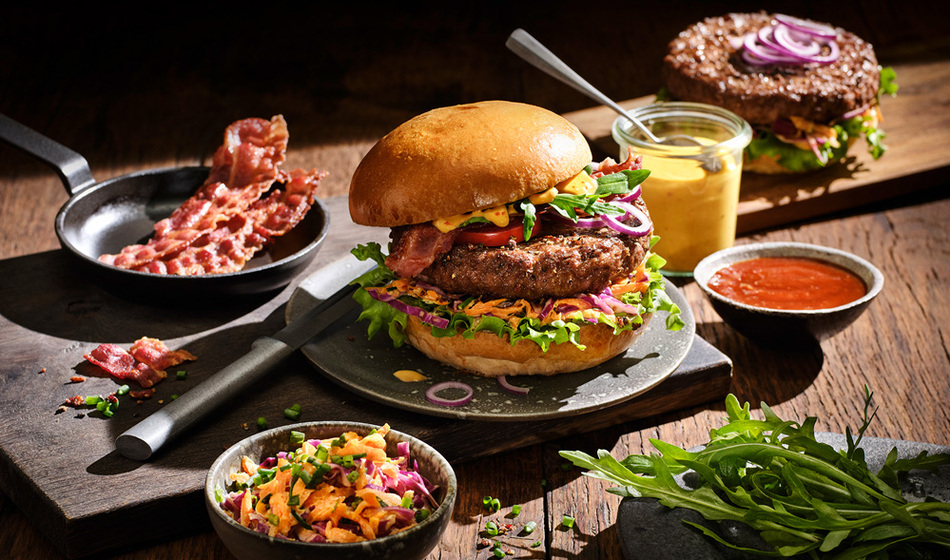 Block House Burger auf einem Teller mit Speckstreifen und Soßen daneben