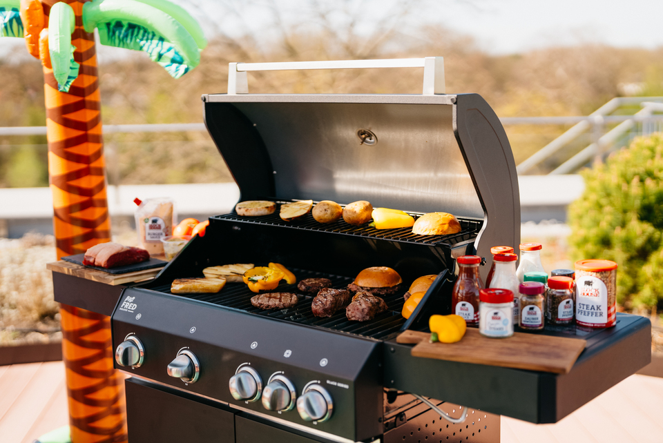 Sommerliches BBQ mit Block House Produkten: Grill mit Burger Patties, Brot, Gemüse und Block House Gewürzen im Freien.
