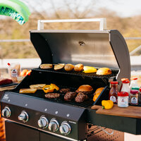 Sommerliches BBQ mit Block House Produkten: Grill mit Burger Patties, Brot, Gemüse und Block House Gewürzen im Freien.