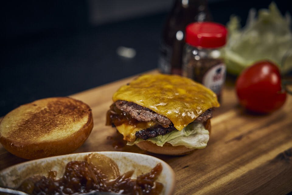 Frisch gegrillter Block House Burger mit doppelt geschmolzenem Cheddar, Salat und Zwiebeln auf einem Holzbrett, bereit zum Servieren.