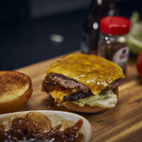 Frisch gegrillter Block House Burger mit doppelt geschmolzenem Cheddar, Salat und Zwiebeln auf einem Holzbrett, bereit zum Servieren.